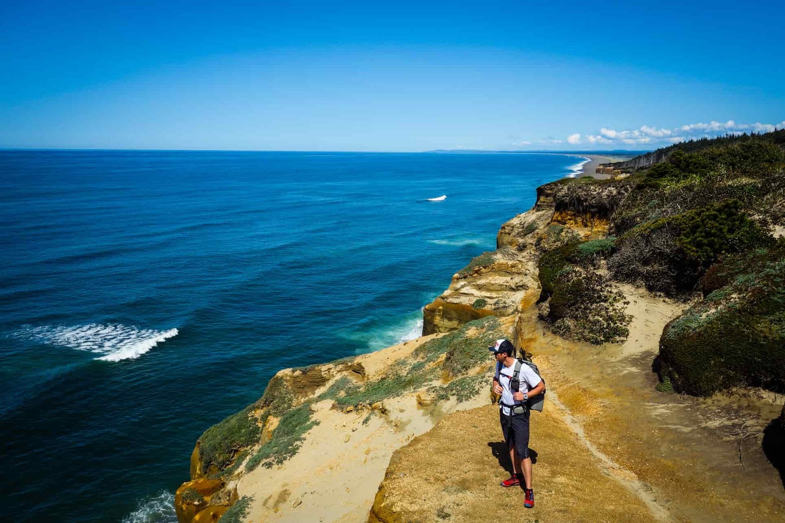 backpacker standing on a tall cliff providing expansive oregon coast views, bright blue pacific ocean, and bluebird skies.