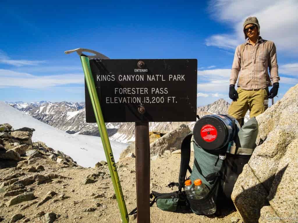 An ice axes rests on a sign for Kings Canyon National Park as a hiker looks on