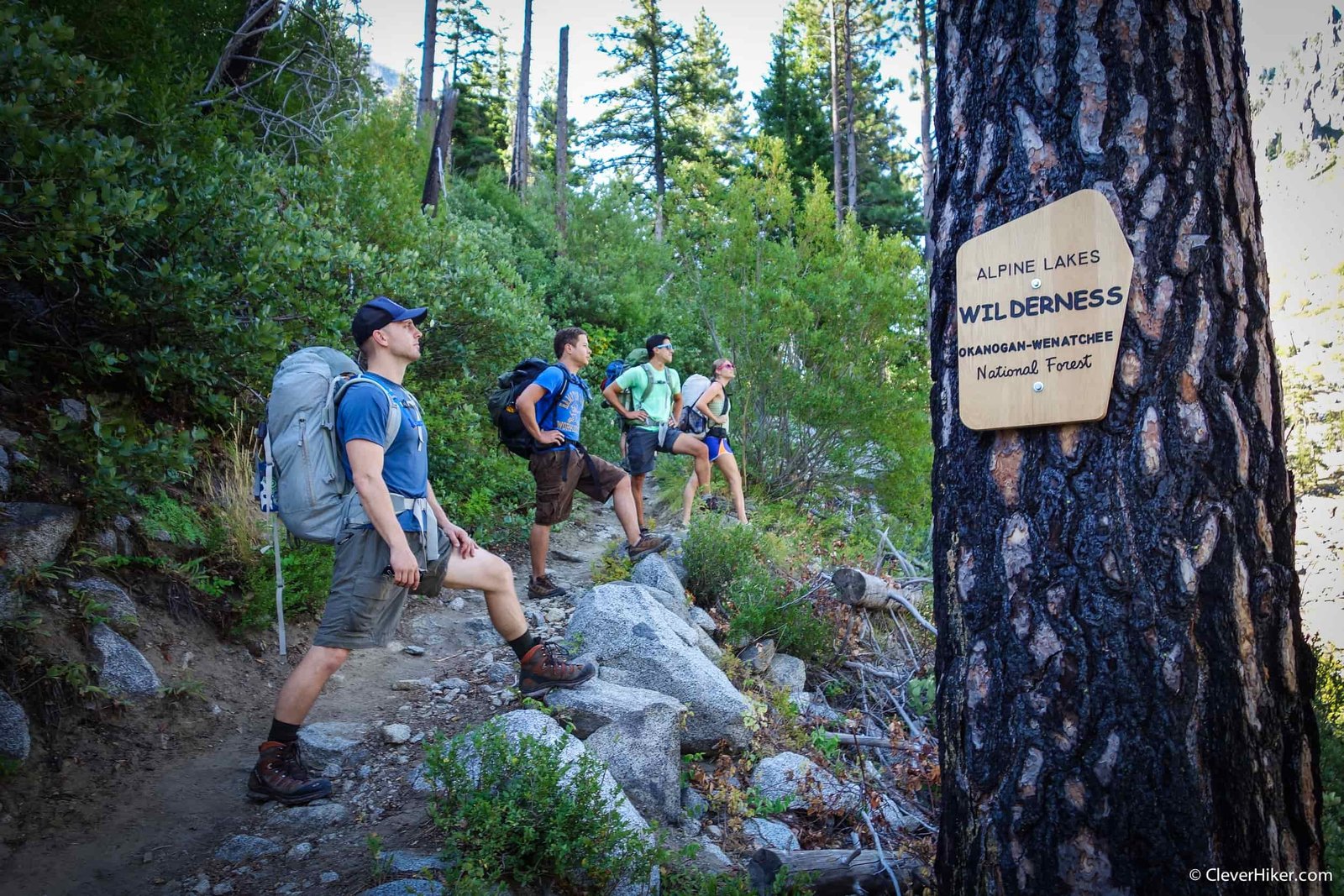 backpackers posing on a trail with a sign indicating that says alpine lakes wilderness