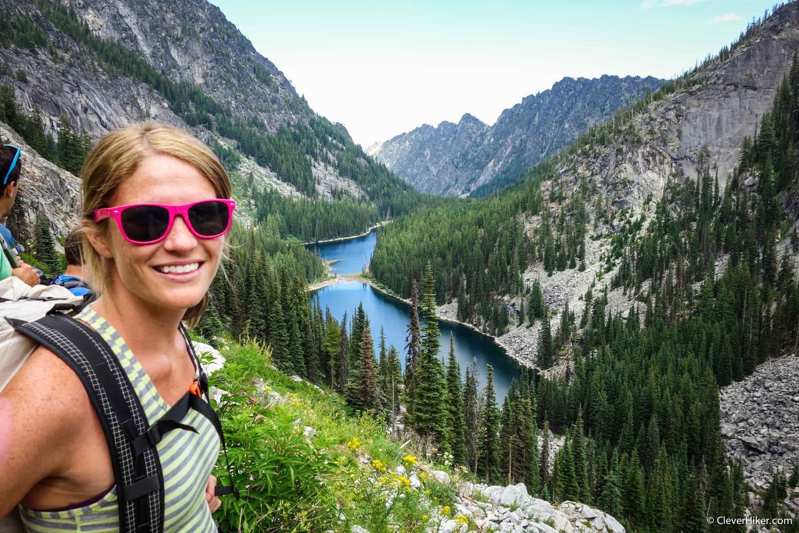 woman posing with sunglasses on with an apline lake in the background