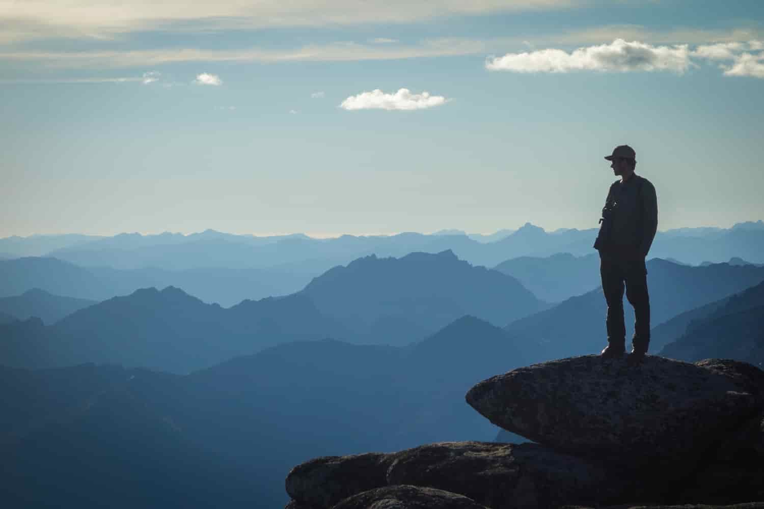a man standing in the foreground with mountains layered in the horizon