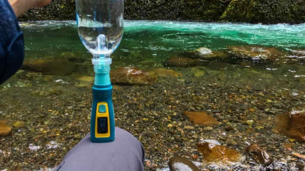 a backpacker with the katadyn steripen inserted into a waterbottle next to a clear blue green river