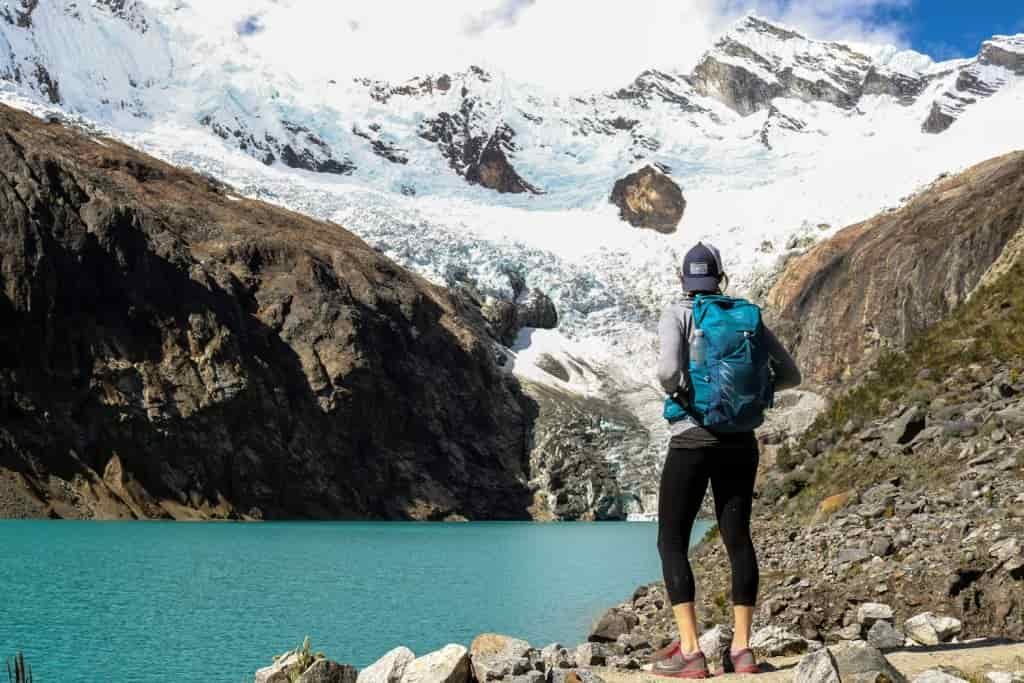 A female hiker stares at a glacier over another alpine lake in Peru