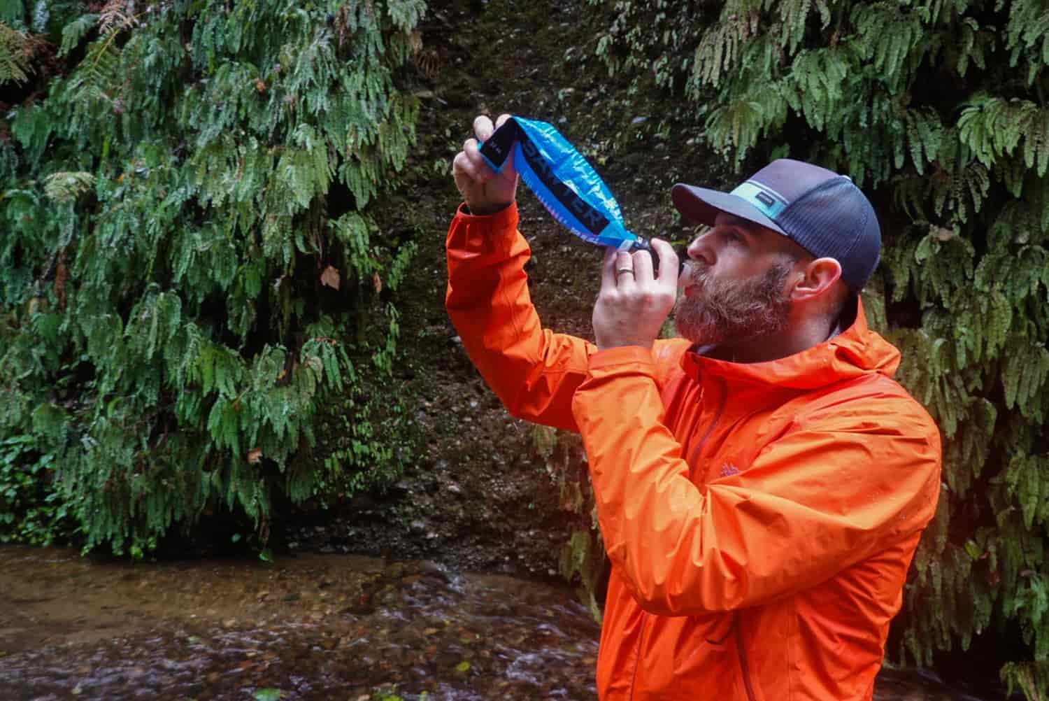 Backpacker drinking from a filter connected to a squeeze pouch to filter the stream water so it is safe to drink