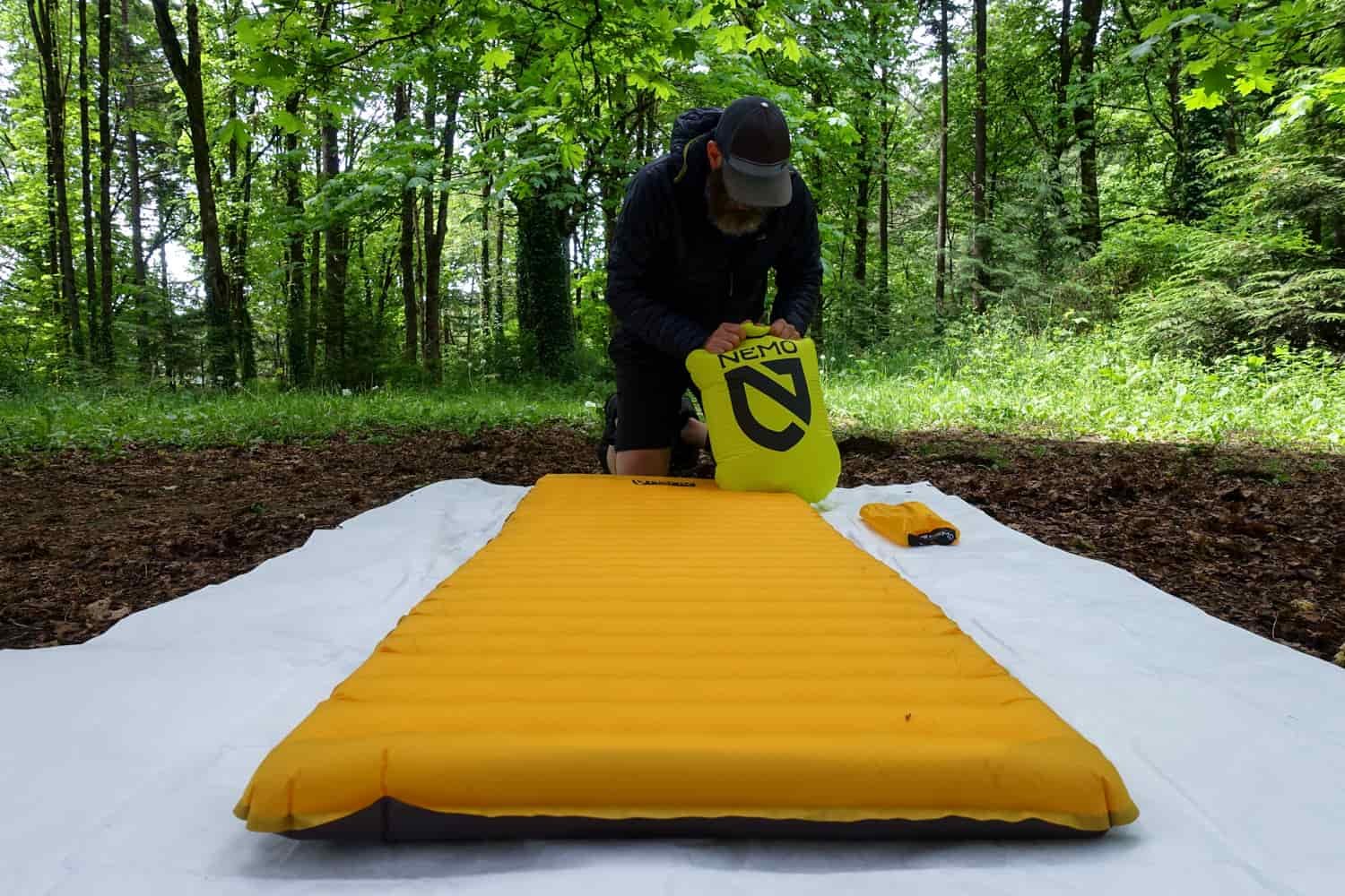a backpacker inflating the NEMO tensor trail ultralight with a pump sack outside under a green canopy forest.