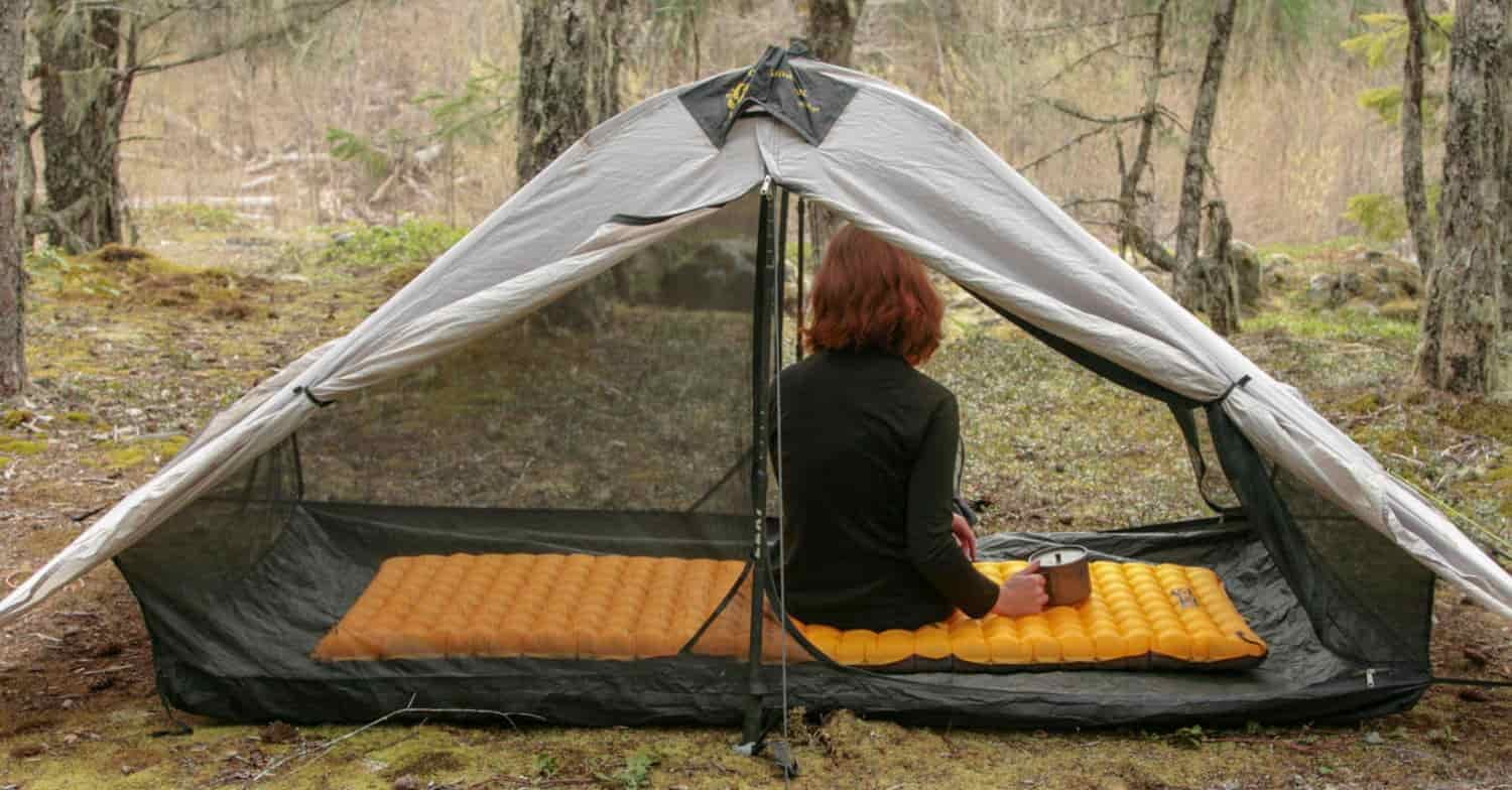 a women sits on top of her NEMO tensor trail ultralight while inside her tent in the forest
