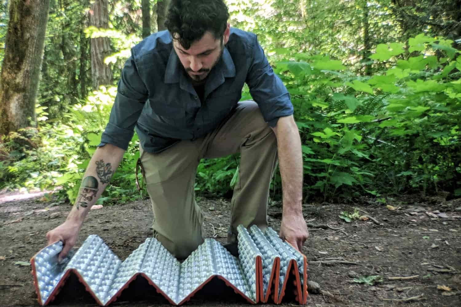 a camper shows the acordian folding pattern on the NEMO switchback while kneeling on the ground in a green forest