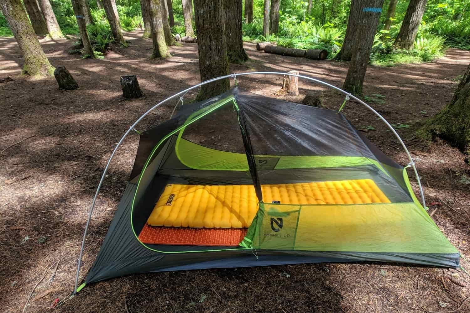a tent in a campsite under a forest that has two sleeping pads stacked on top of each other. One is a closed cell foam pad and the one on top is an insulated air pad, both by NEMO equipment.