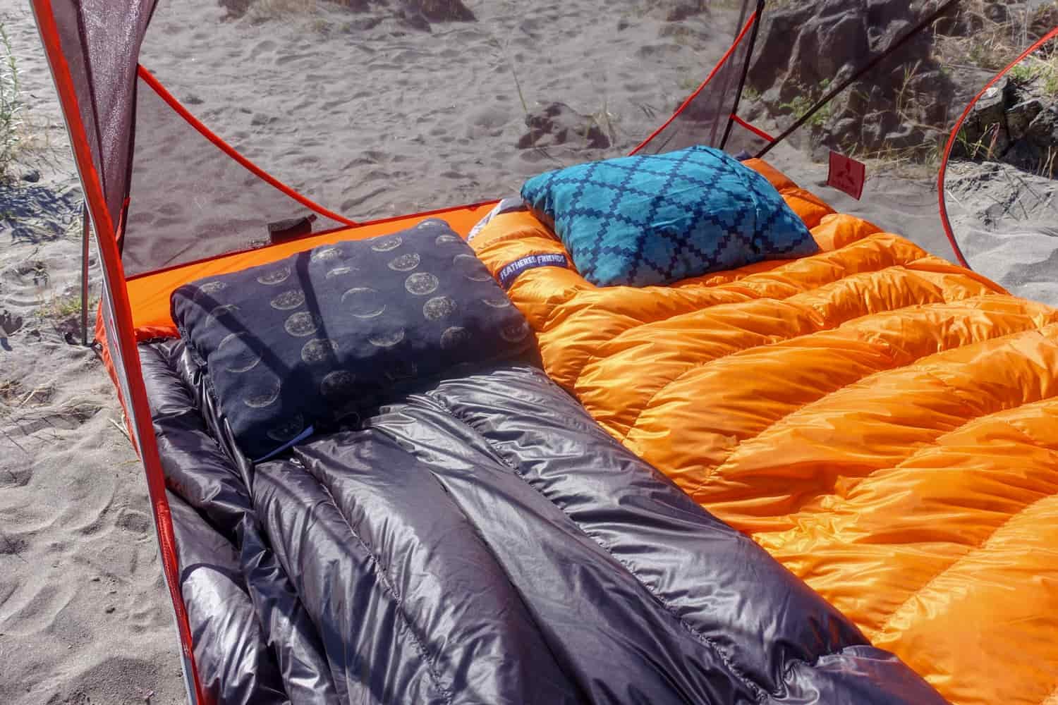Close-up shot of two sleeping bags setup with pillows inside a tent with no fly on.