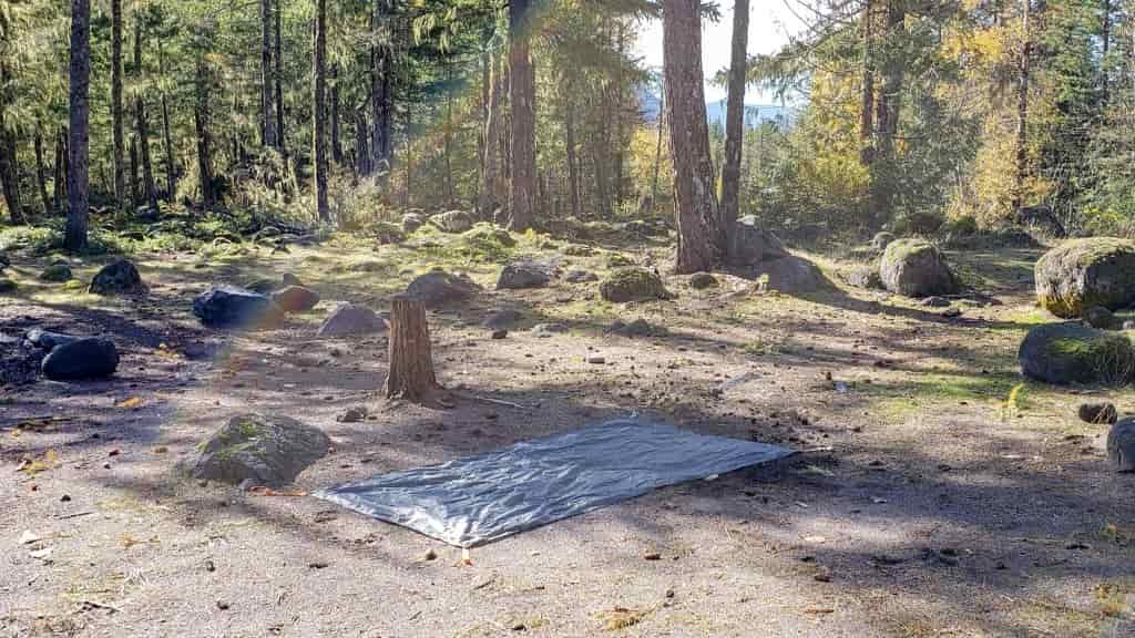a tent footprint spread out on the ground at a flat campsite with plenty of pine cones on the ground