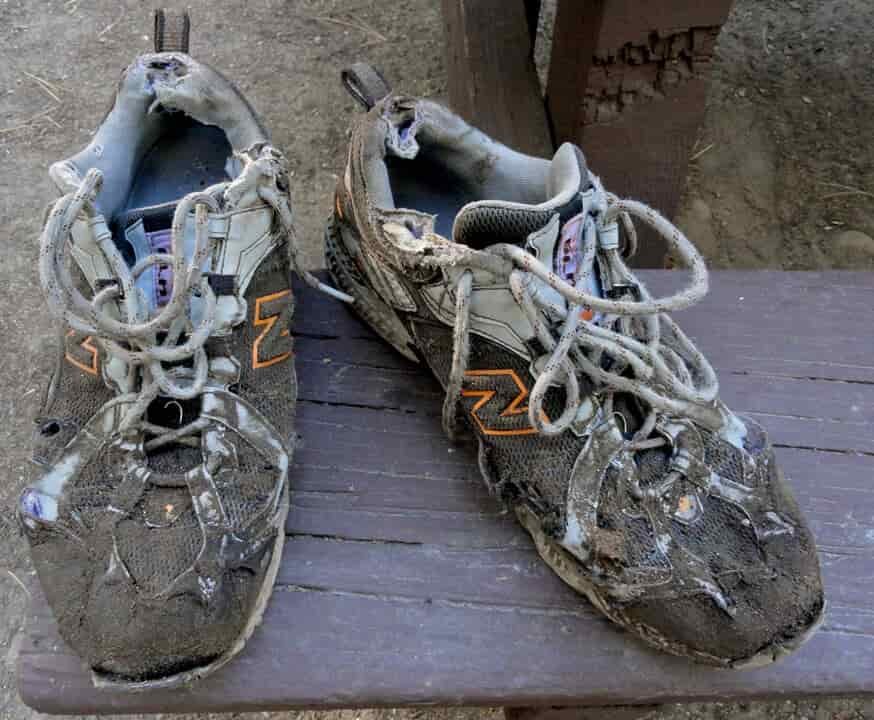 an extremely beat up and hole ridden pair of trail running shoes on a table