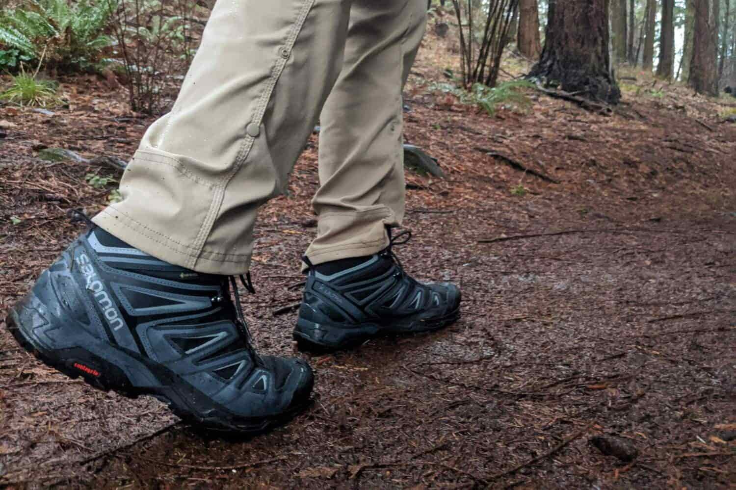 salomon black boots are in the forefront of the frame on a man walking away on a dirt path