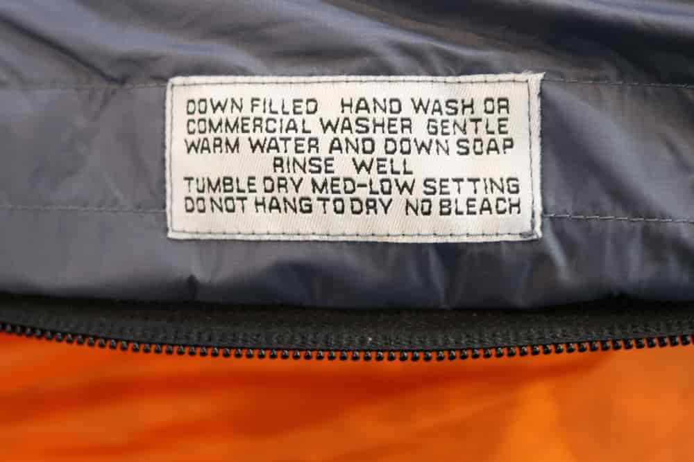 A care label inside a sleeping bag reads "DOWN FILLERED HAND WASH OR COMMERCIAL WASHER GENTLE WARM WATER AND DOWN SOAP RINSE WELL TUMBLE DRY MED-LOW SETTING DO NOT HANG TO DRY NO BLEACH