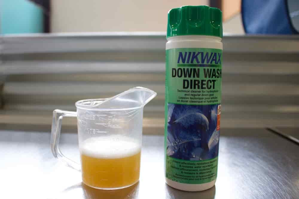 A measuring cup filled with down wash direct sits next to a bottle of Nikwax Down Wash Direct 