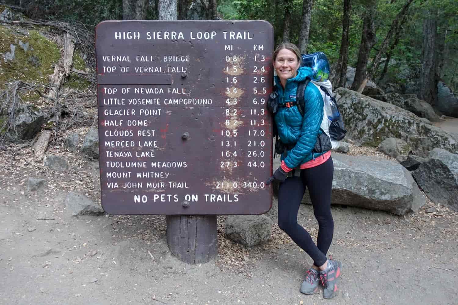 hiker posing in front of a yosemite national park trail information sign