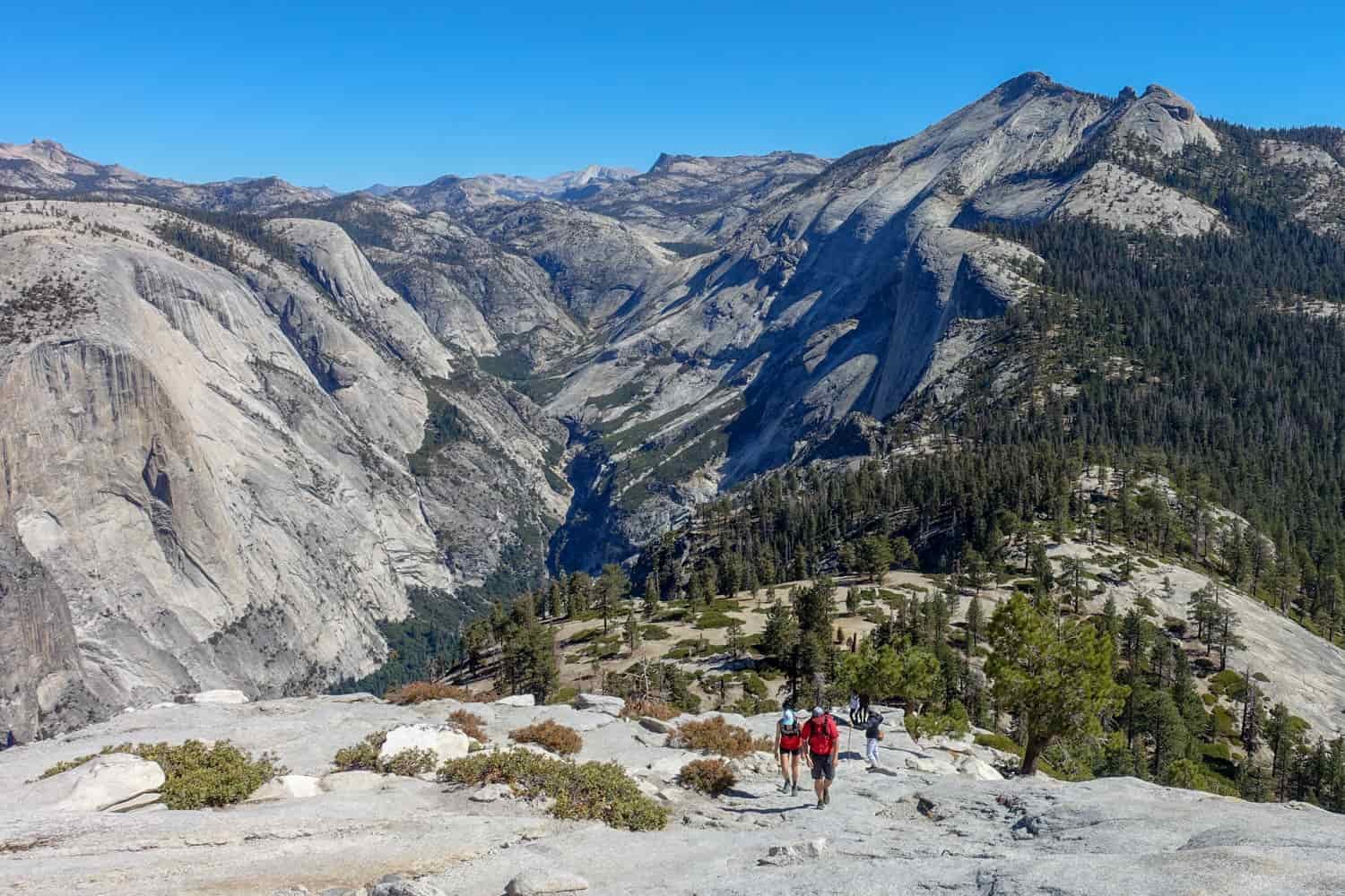 hikers walking up the base of half dome with yosemite valley in the background