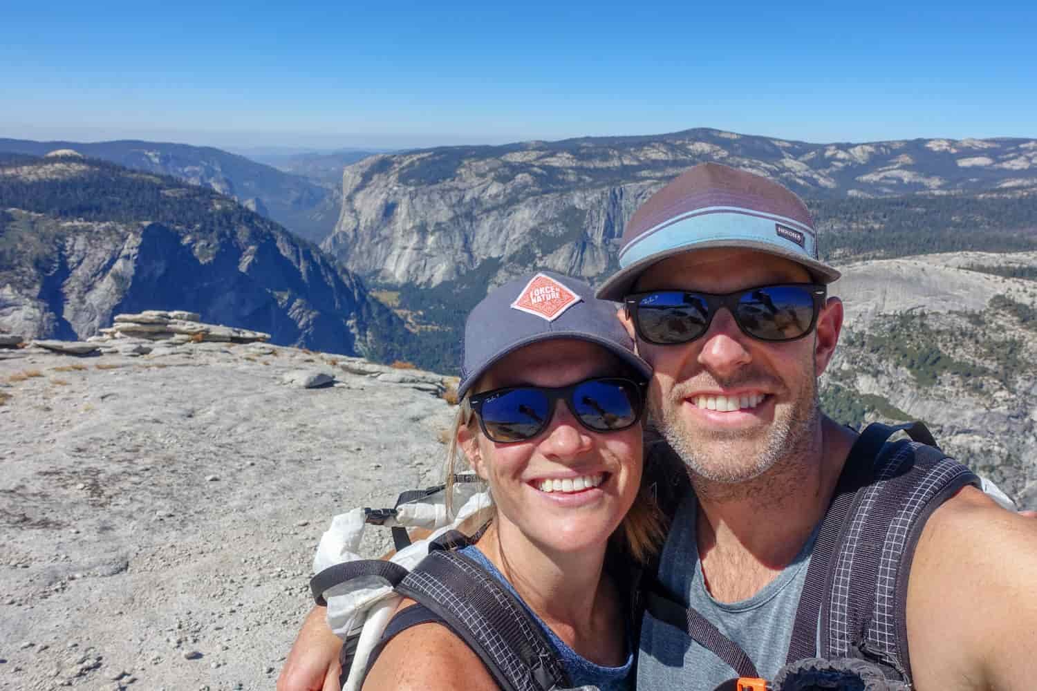 two hikers taking a selfie on top of half dome in yosemite