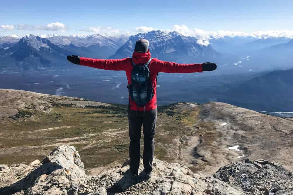 Rear view of a hiker standing on a mountain summit with his arms spread wide
