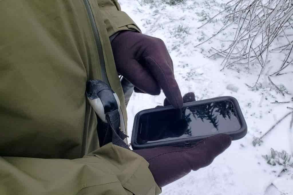A woman touches the screen of her cell phone while wearing gloves 