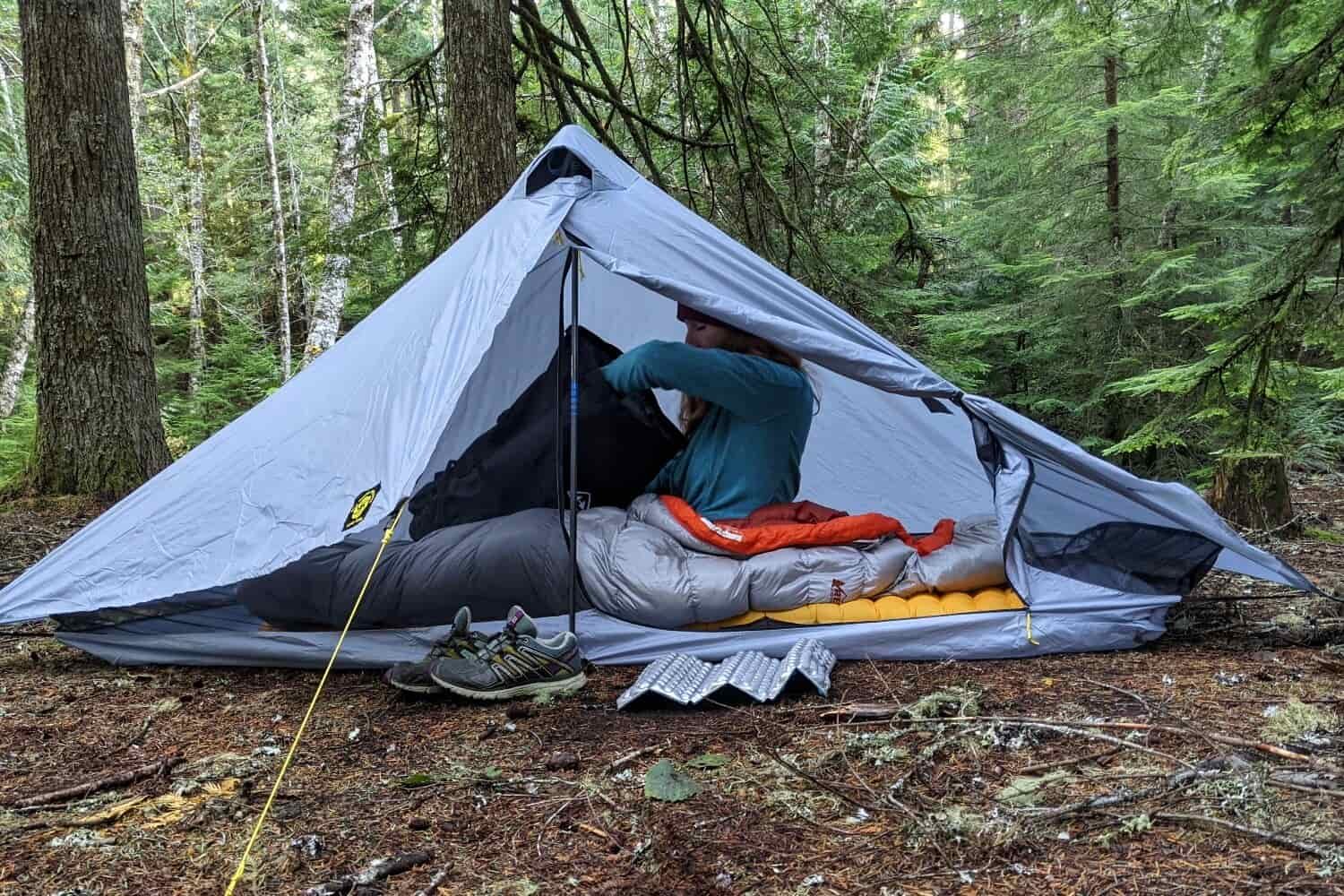 A hiker sitting inside the Six Moon Designs Lunar Solo Tent digging through a backpack
