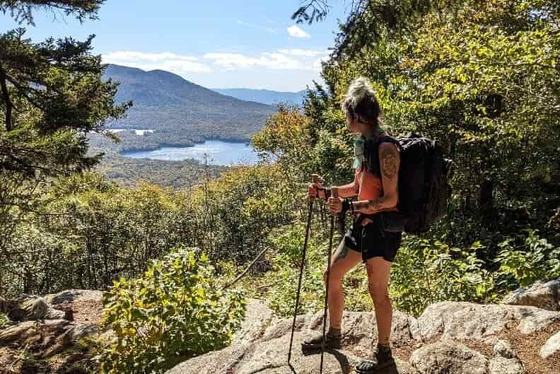 hiker standing on a rocky vista looking over a wooded lake with gossamer gear trekking poles in her hands