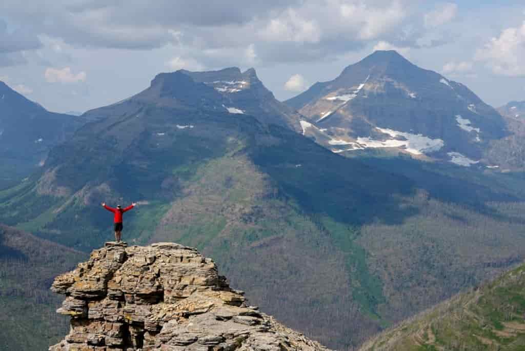 A hiker poses on a rocky outcrop overlooking a stunning valley of mountains