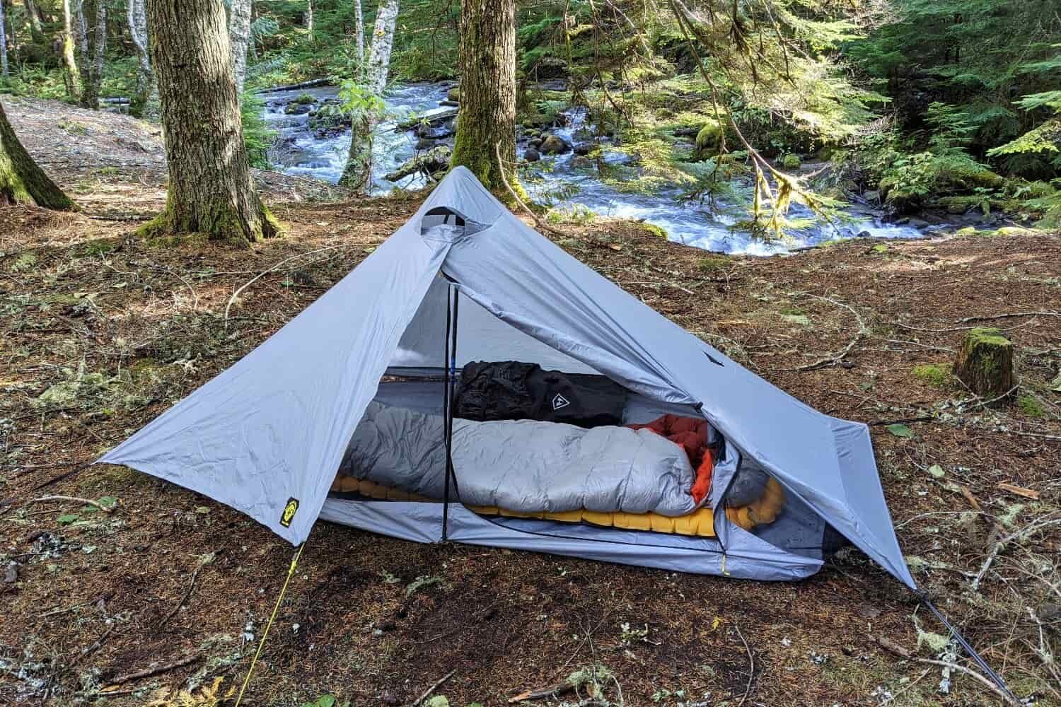 a six moon designs lunar solo tent set up in front of a river the door is open to show how much space for sleeping and gear is inside