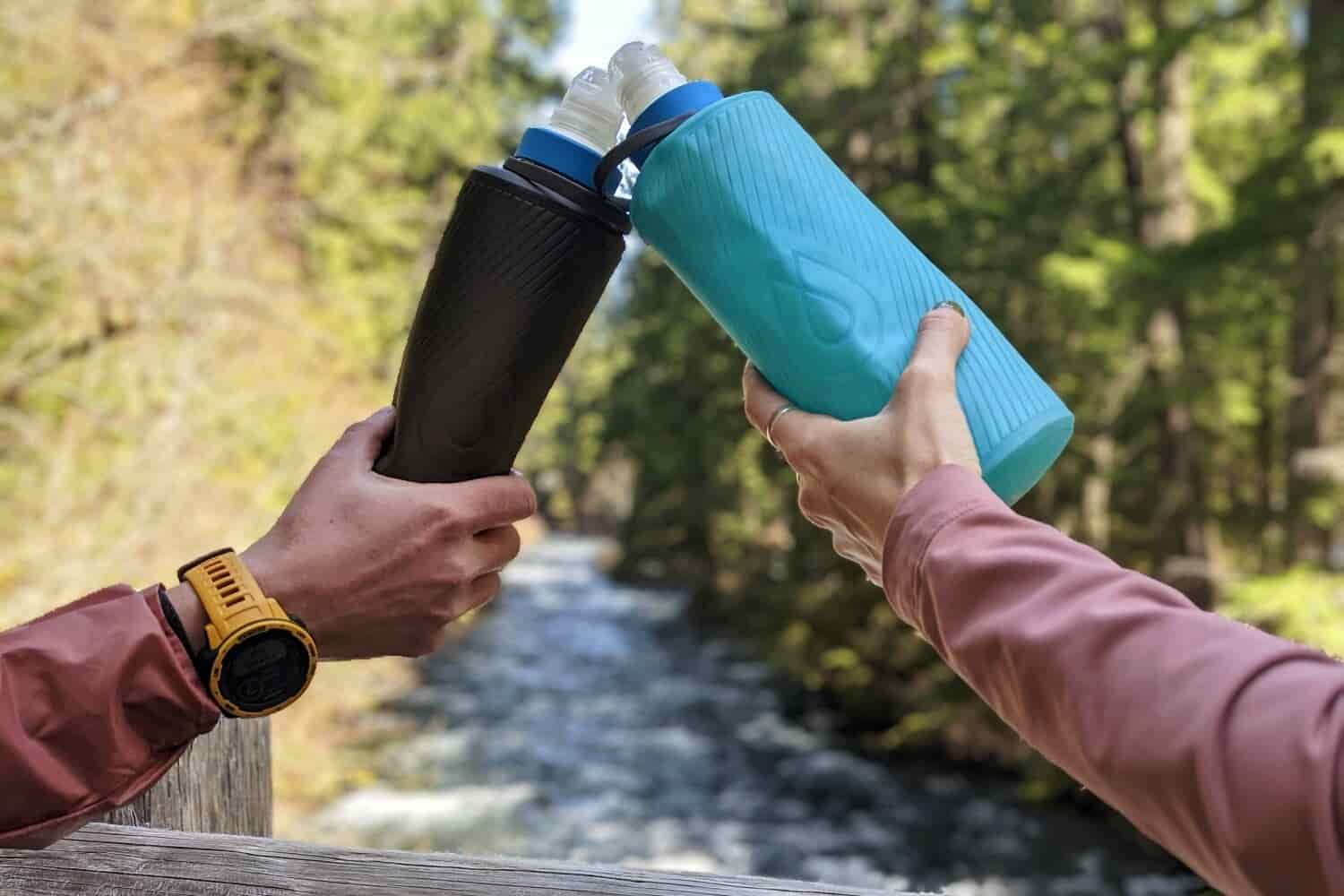 Two backpackers cheers their lightweight water filter bottle systems over a river