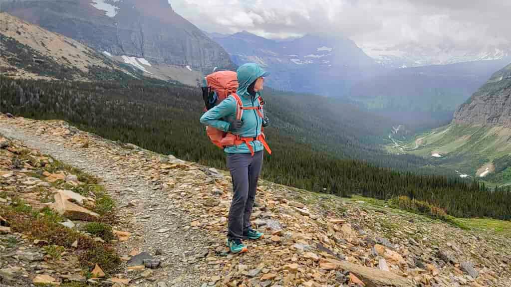 A backpacker wearing the Black Diamond Alpine Start Windbreaker while hiking in Glacier National Park in June