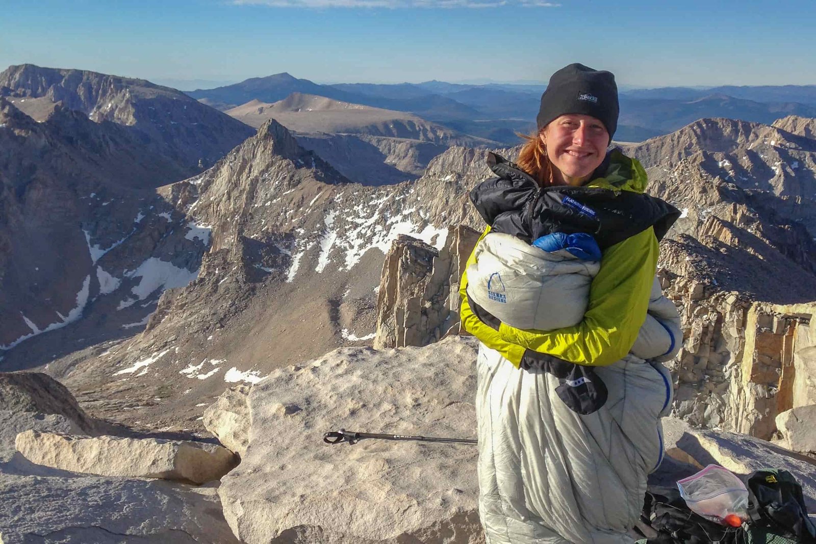a female backpacker stands on a mountain wrapped in her sleeping bag