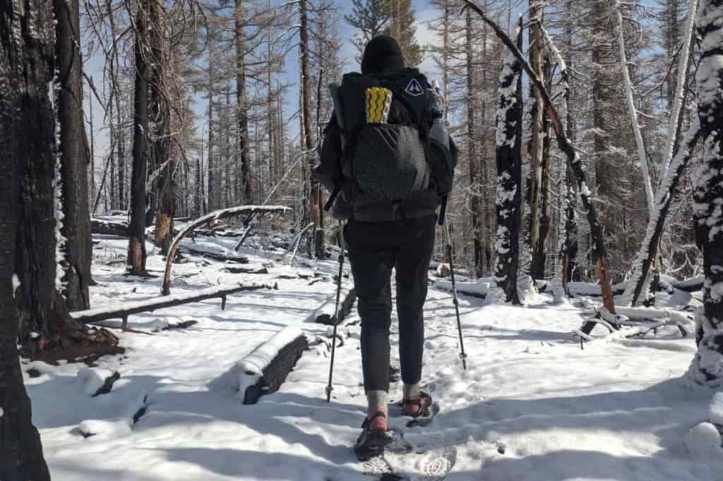 A hiker walks through shallow snow wearing hiking socks under hiking sandals
