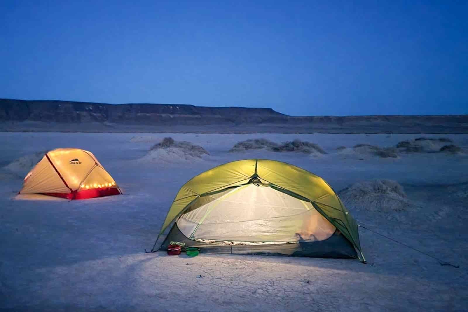two backpacking tents with interior camping lights turned on while set up on a desert playa