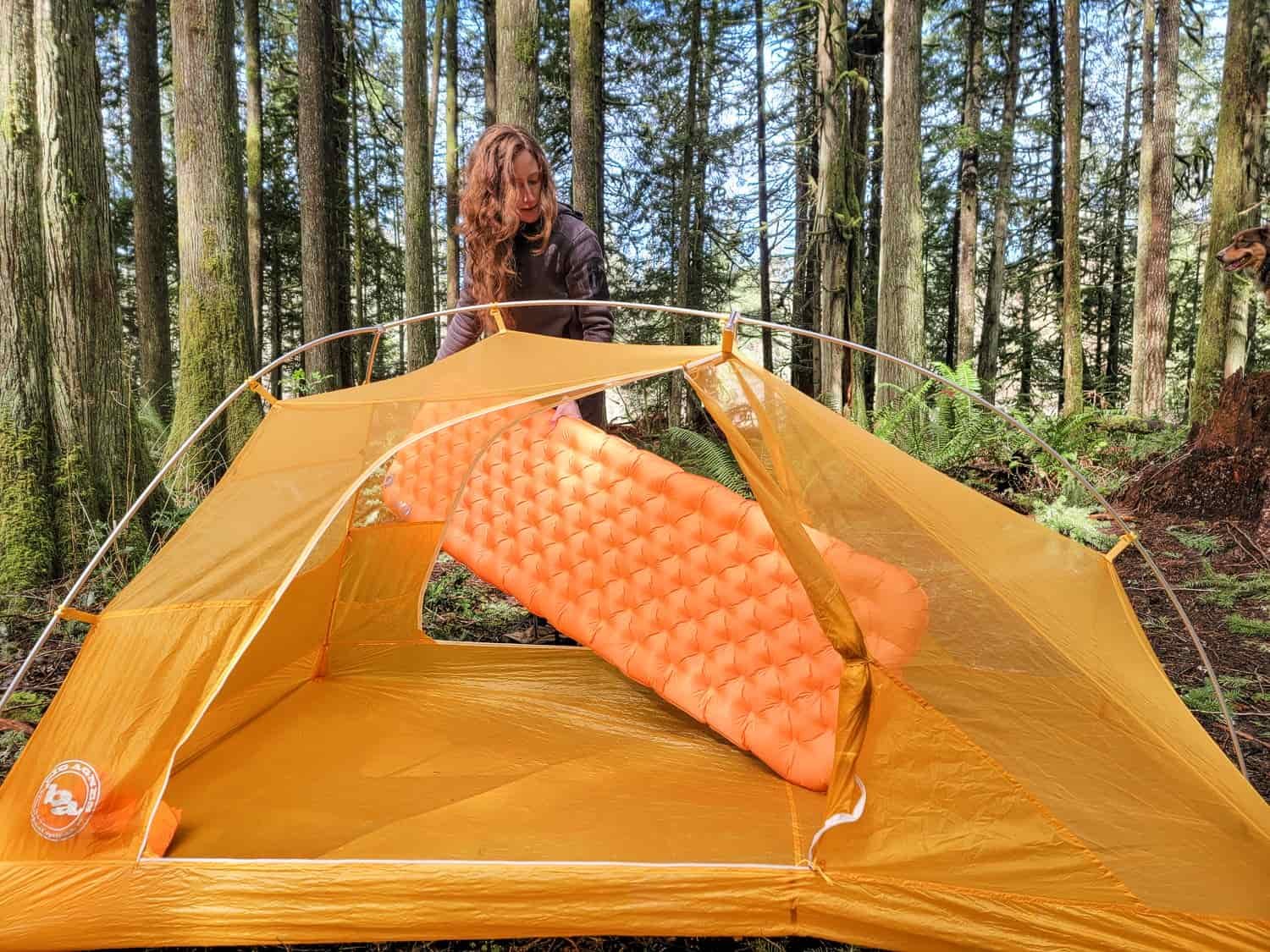 a backpacker sets up their sleep system with a tent and a sleeping pad. They are placing the inflated pad inside the tent through the open door.