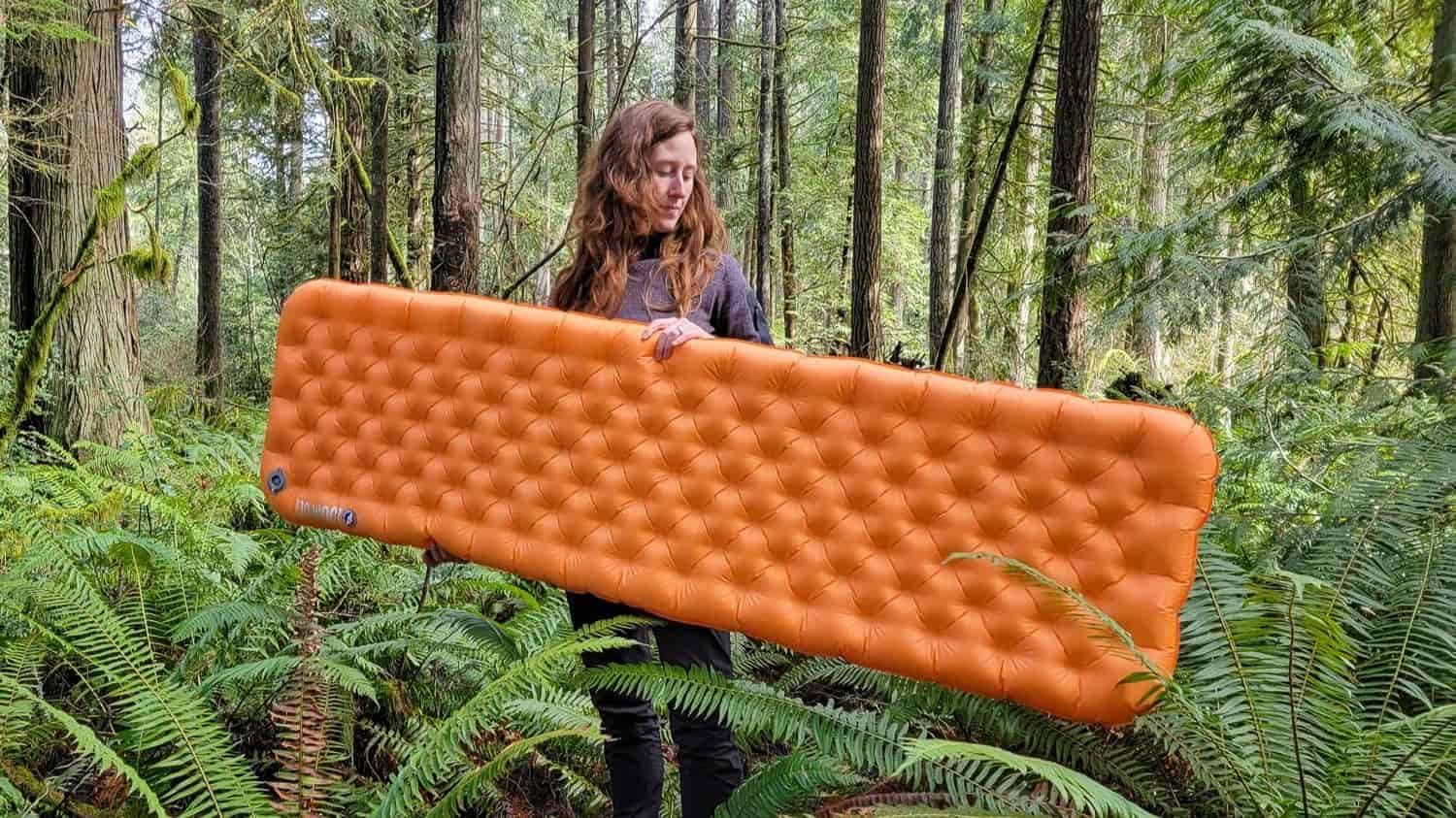 a woman standing in fern covered understory in a mossy covered forest holding the Big Agnes Zoom Ultralight inflated sleeping pad in her hands