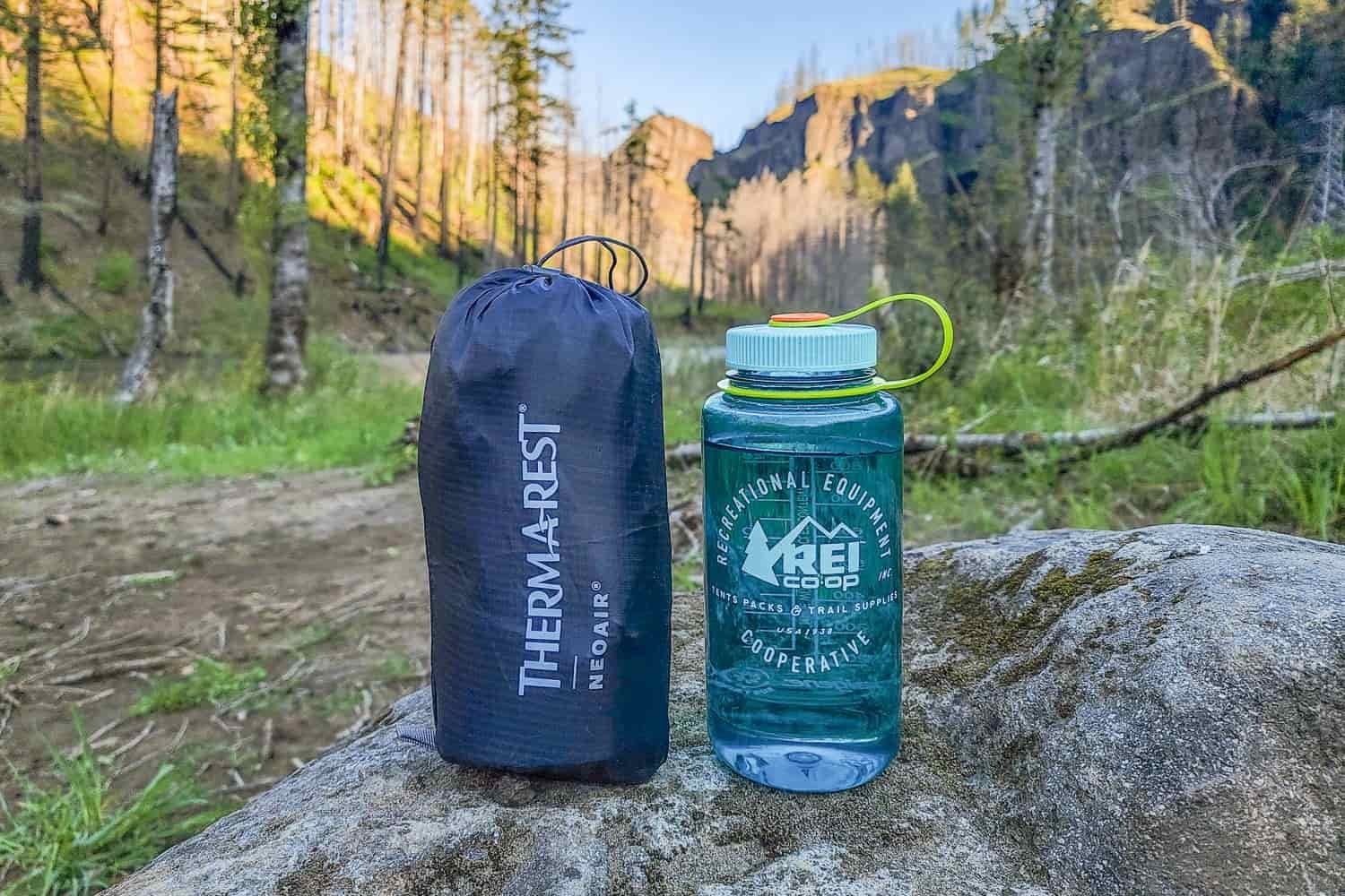 a Therm-a-rest Xlite NXT packed sleeping pad in its compression pack next to a nalgene bottle in a forested valley showind the size is about the same
