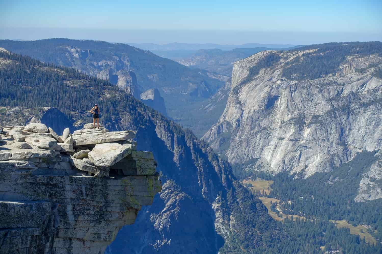 hiker posing on an undercut ledge on top of half dome in yosemite