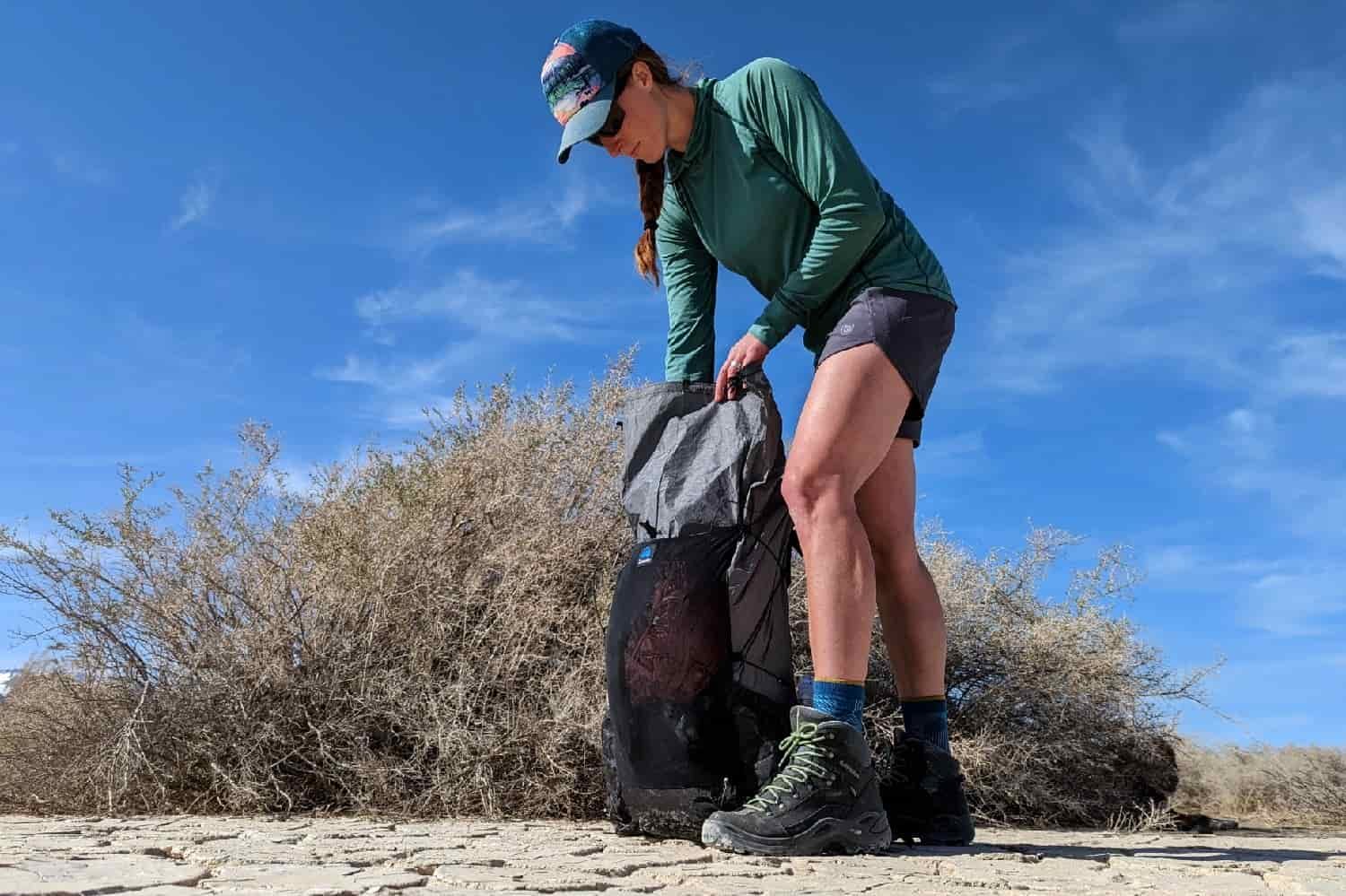 woman wearing a suns shirt packing a backpack on a desert playa