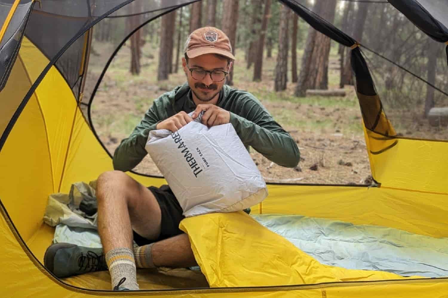 A hiker blowing up the NeoAir XLite NXT with a pump sack while sitting inside a tent in the wilderness.