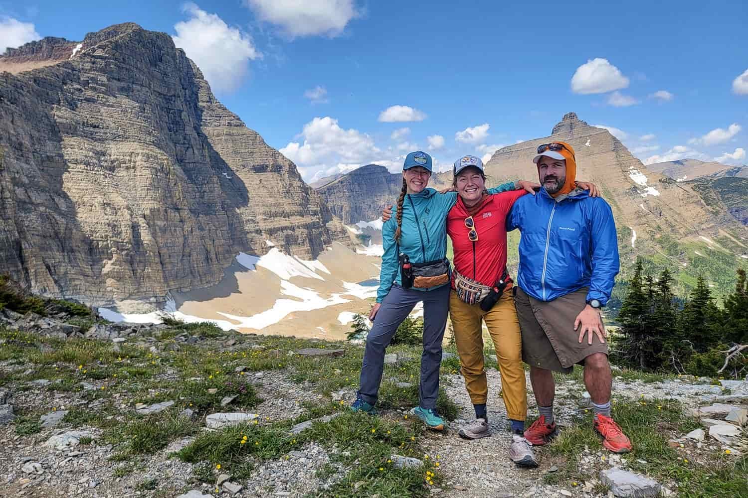 Two women and a man pose on a trail with mountains in the background