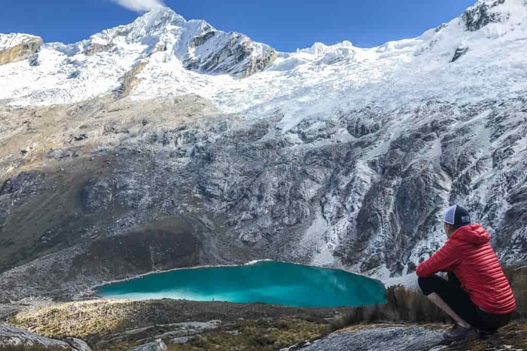 A female hiker looks down on an aquamarine lake from high on a mountain