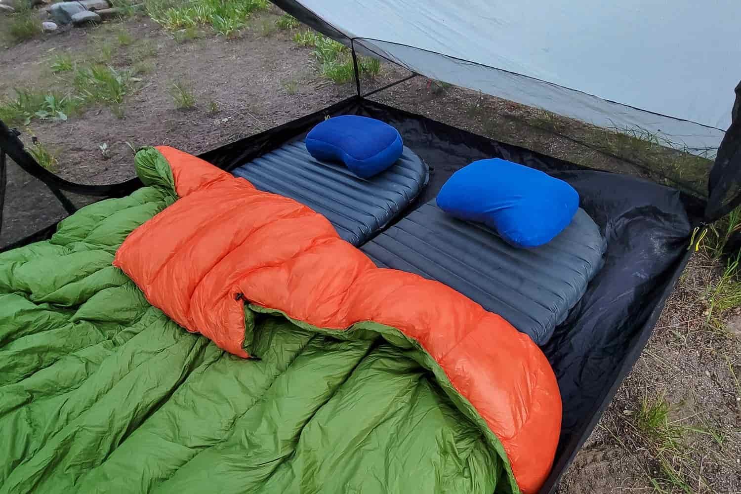 Two pads with sleeping bags and pillows in a tent.