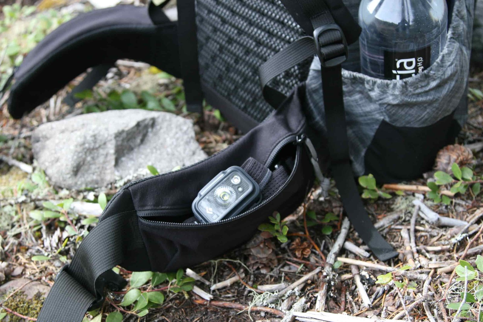 a backpack with a hip belt pocket is open and contains a small black headlamp
