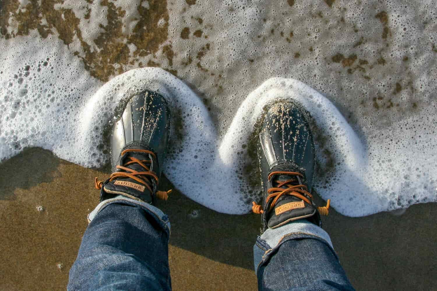 sperry saltwater duck boots in the foamy surf on the beach
