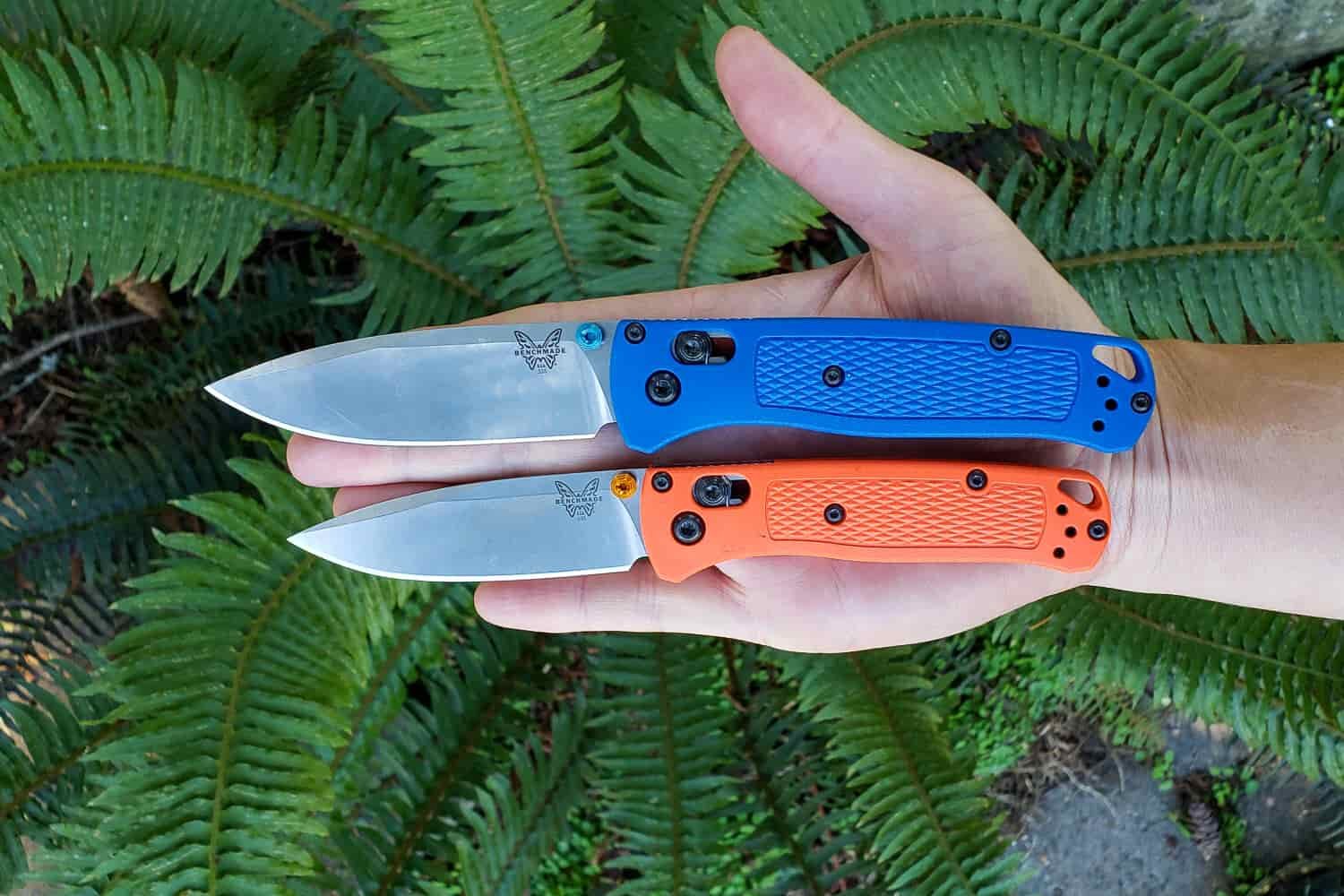 a hiker holds two pocket knives made by bugout in their hand to compare sizes