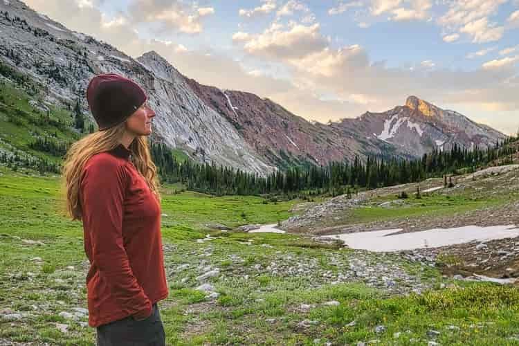 Profile of a female hiker in a red beanie and lightweight red fleece top as she looks over a meadow