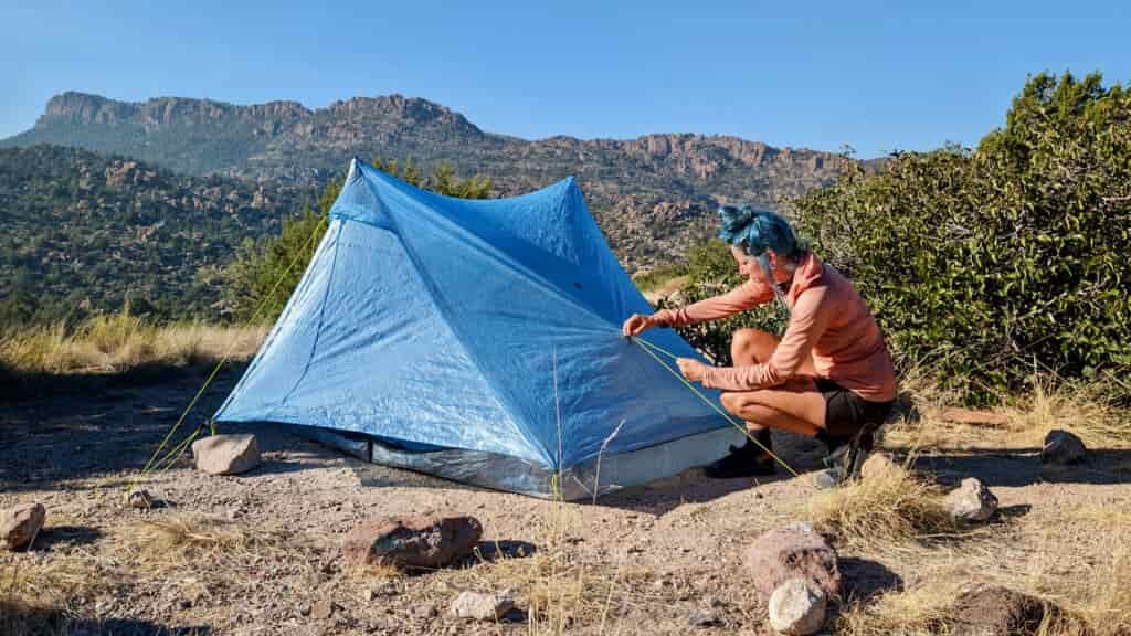A hiker adjusting the Zpacks Duplex Zip in a plateau with mountains in the background.
