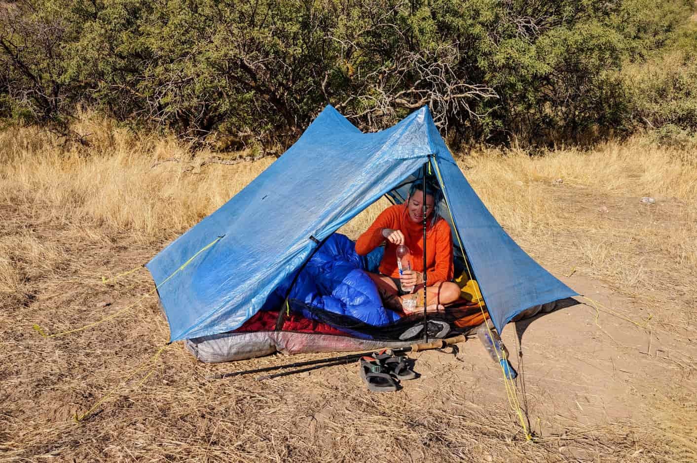 A backpacker sitting inside the Zpacks Duplex Zip tent in a sunny field with desert trees in the background