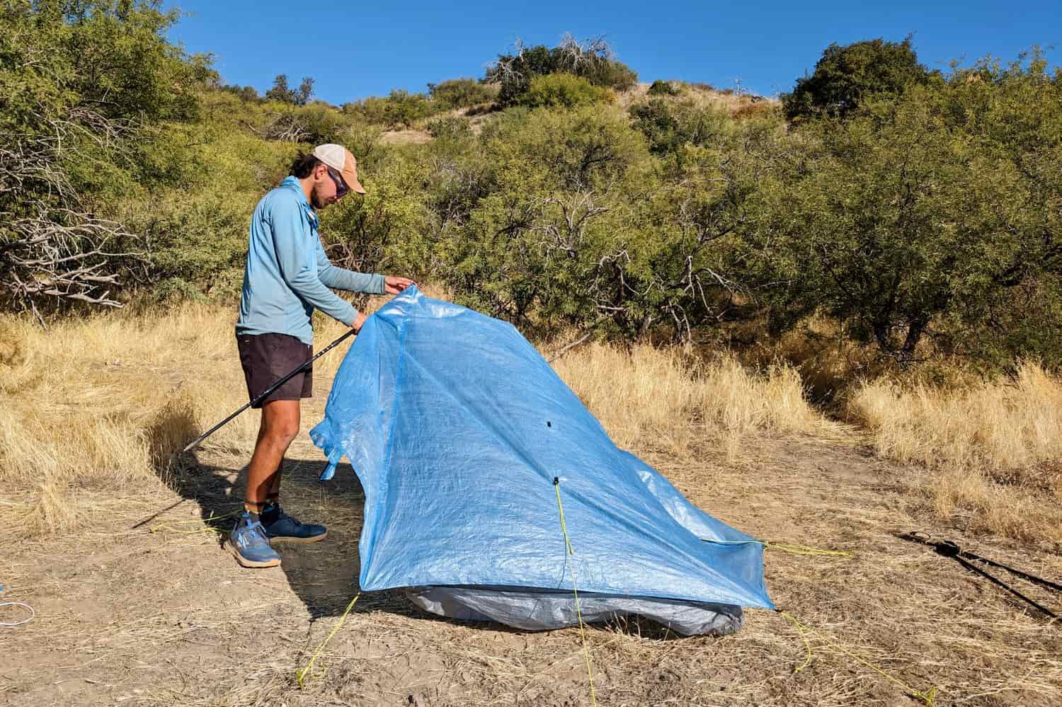 A hiker setting up the Zpacks Duplex Zip tent using trekking poles to prop up one side of the tent 
