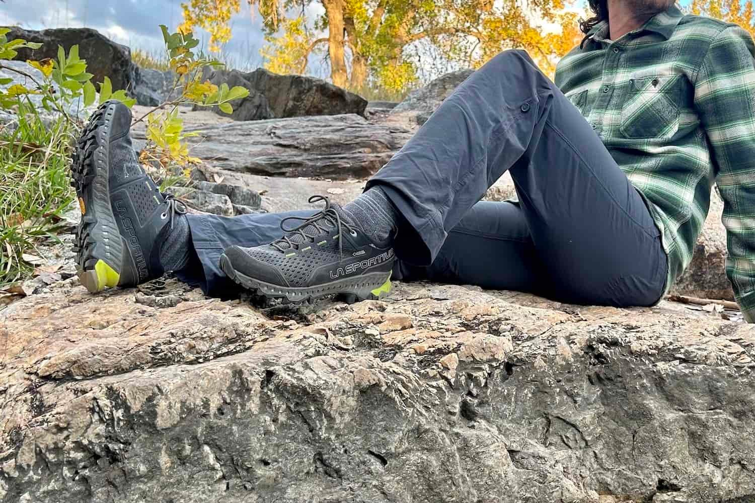 The lower half of a male hiker sitting on a rocky slab in hiking pants and the La Sportiva Spire GTX hiking shoes
