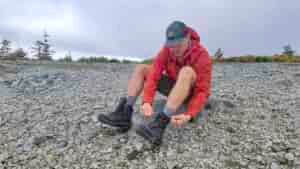A hiker in a red rain jacket sitting on a rock to tie his Salomon Quest 4 GTX boots